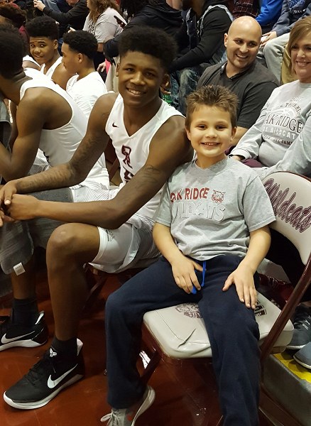 AJ Cucksey, a six-year-old cancer survivor and kindergarten student at Farragut Primary, sits on the Oak Ridge Wildcats sideline next to senior Tee Higgins (5), who dunked for AJ during a 68-38 win over West during a Region 2-AAA quarterfinal game at Wildcats Arena on Saturday, Feb. 25, 2017.