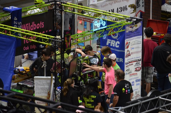 Members of the Secret City Wildbots crew work on Luna, the 2017 robot, during the opening practice matches on Thursday, March 23, 2017. At left (in black long sleeves) is Eric Thornton; center (also in black) is Jacob LaRose, Luke Buckner (next in yellow) as a graduate advisor, Caden Webb (in pink), mentor Chuck Agle (in black, back to camera), and Olivia Mahathy (in black, back to camera). (Photo by Angi Agle)
