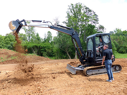 Energy Secretary Rick Perry operates an excavator that has 3D-printed parts (the cab, a heat exchanger, and the last section of boom before the bucket) at Oak Ridge National Laboratory's Manufacturing Demonstration Facility on Hardin Valley Road on Monday, May 22, 2017. Perry receives instructions from MDF technician Matt Sallas. (Photo by John Huotari/Oak Ridge Today)