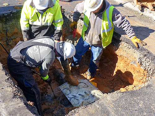 An Oak Ridge Public Works Department crew repairs a broken water line underneath Northwestern Avenue near Nevada Circle at lunchtime Saturday, Jan. 6, 2018. The crew here is supervised by Oak Ridge Public Works Department Utility Line Maintenance Crew Chief Michael Brown, in front. Also pictured are Water Specialist Gene Wilson, left, and Maintenance Mechanic Jeremy Justice. (Photo by John Huotari/Oak Ridge Today)