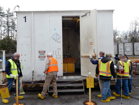 Workers prepare to install vents in drums of legacy transuranic waste in a closed, explosion-proof, high-efficiency particulate air-ventilated unit to ensure safety of workers and the environment. (Photo courtesy U.S. Department of Energy Office of Environmental Management)