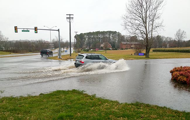 A vehicle drives through flood water pooled at the intersection of Lafayette Drive and Administration Road as heavy rain falls continuously on Tuesday morning, Feb. 12, 2019. (Photo by John Huotari/Oak Ridge Today) 